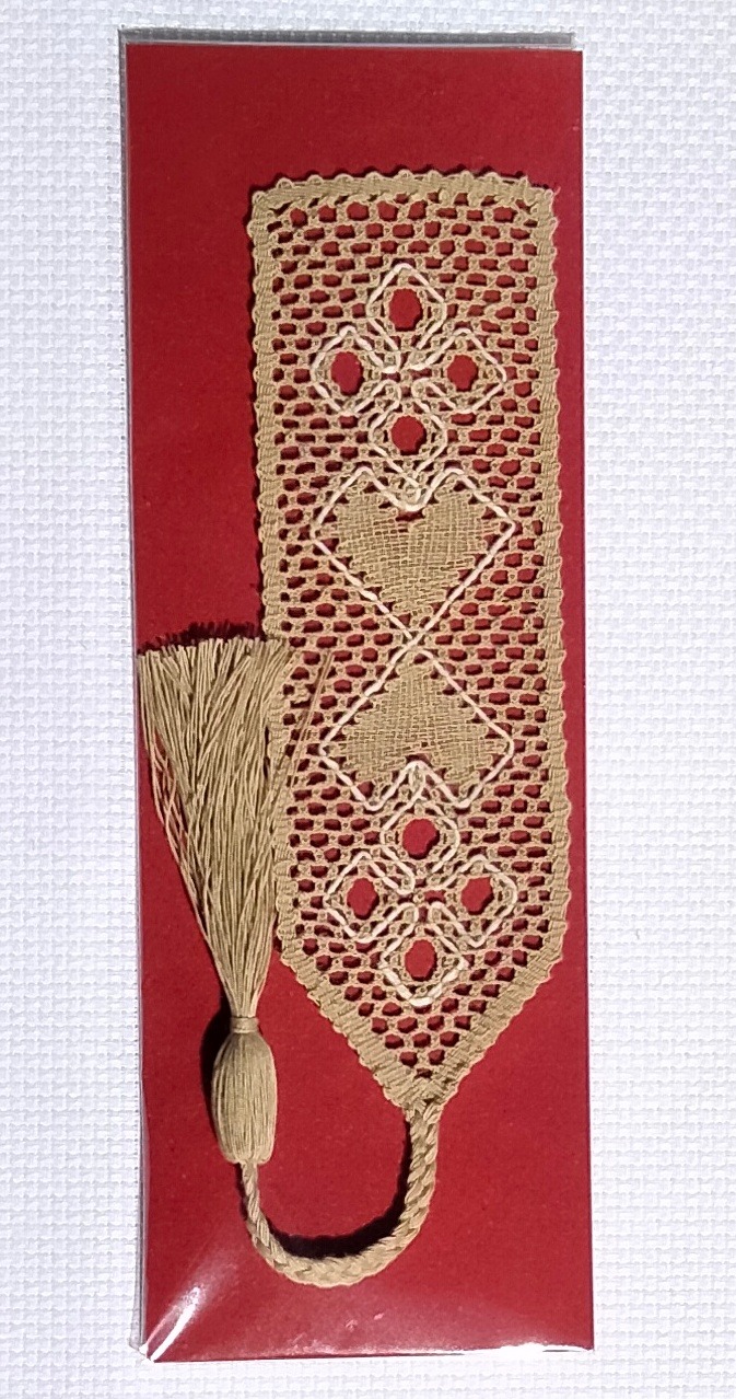 Nyplätty kirjanmerkki "Kaksi sydäntä", päävärinä pellava, kuviota rajaa valkoinen lanka.