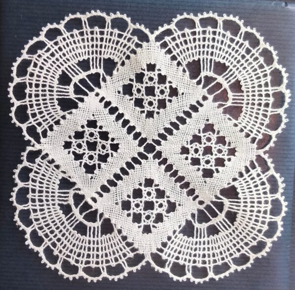 Neliskanttinen nyplätty pellavapitsiliina Piparkehä, valkoinen. Mitat 15x15 cm. Väri: valkoinen. Liinan ulkoreuna koostuu neljästä pyöreästä kulmasta, joita reunustavat pienet, sirot kaaret. Keskiosa on kärjellään seisova neliö, joka koostuu neljästä pienemmästä kuvioidusta neliöstä.