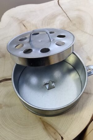 Kannellinen hyttyssavuastia, jossa on sisällä piikki savukierukkaa varten. Kannessa on reikiä. Kahva kannessa ja astian reunassa. Materiaali: galvanoitu pelti. Halkaisija 13 cm, korkeus 4,3 cm