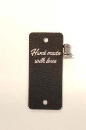 Merkki teksillä "Hand made with love". Musta, tekonahkaa. Merkin voi kiinnittää ja irrottaa ruuvattavalla nastalla. Koko: 2,5 cm x 5,8 cm