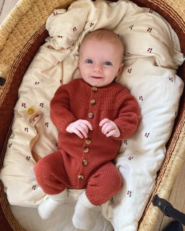 PetiteKnit Anker´s Onesie. Kuvassa vauva hymyilee korivuoteessa.