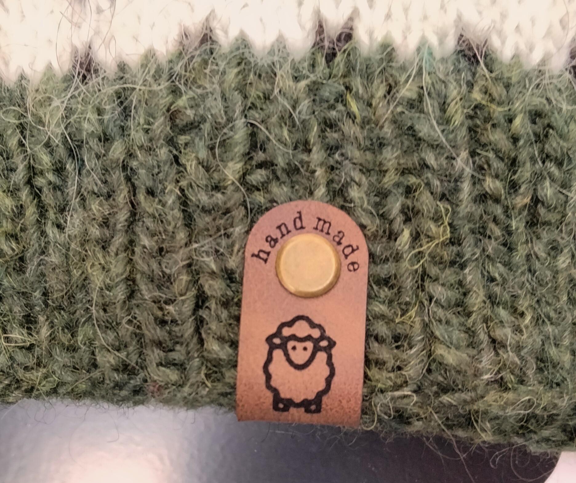 Handmade-merkki kiinnitettynä ruuvilla puseron helmassa. Kuviona on lammas.