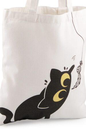 Valkoinen puuvilla kassi. Painatuksessa on musta kissa, joka havittelee narun päässä olevaa lelua. Lelun kuva toistuu kassin toiella puolella.